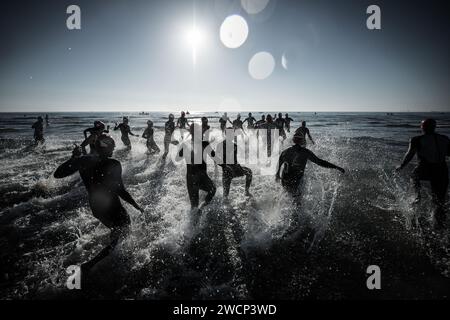Triathleten in Neoprenanzügen, die bei einem wunderschönen Sonnenaufgang ins Meer laufen, um den Wettkampf am Strand von Malvarrosa in Valencia, Spanien, zu starten Stockfoto