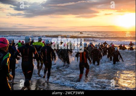Triathleten in Neoprenanzügen, die bei einem wunderschönen Sonnenaufgang ins Meer laufen, um den Wettkampf in Burriana, Castellon, Spanien, zu starten Stockfoto