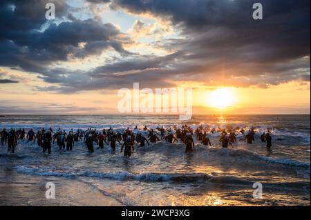 Triathleten in Neoprenanzügen, die bei einem wunderschönen Sonnenaufgang ins Meer laufen, um den Wettkampf in Burriana, Castellon, Spanien, zu starten Stockfoto