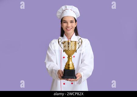 Weibliche Köchin mit goldener Tasse auf lila Hintergrund Stockfoto