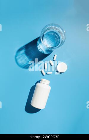 Ein weißes Gefäß, weiße Kapseln mit Vitaminen oder Arzneimitteln und ein Glas Wasser. Arzneimittel Stockfoto