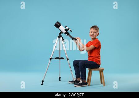 Glücklicher kleiner Junge mit Teleskop auf hellblauem Hintergrund Stockfoto