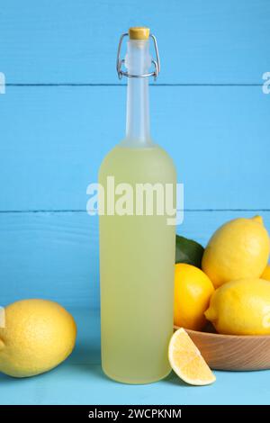 Flasche leckerer Limoncello-Likör und Zitronen auf hellblauem Tisch Stockfoto