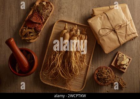 Ein Bambustablett mit Ginseng, auf dem einige Arten traditioneller Medizin und einige Packungen auf Holztisch ausgestellt sind. Naturmedizinischer Gehalt Stockfoto