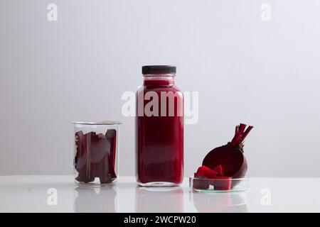 Eine Glasflasche ohne Etikett, gefüllt mit Rote-Bete-Saft. Becher und Petrischale mit Rote-Bete-Scheiben angezeigt. Rote Bete (Beta vulgaris) kann die musc verbessern Stockfoto