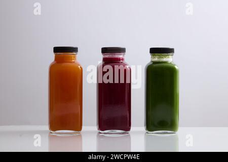 Vorderansicht von drei Glasflaschen mit leerem Etikett, gefüllt mit Saft in Orange, Rot und Grün. Mockup-Design gesunder Getränkemarken. Bio-Saft Stockfoto