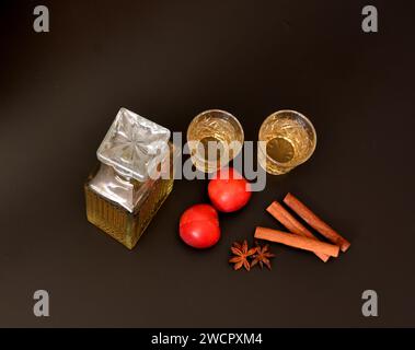 Pflaumenlikör mit Gewürzen, starker hausgemachter Alkohol in einer Kristallkaraffe und zwei Gläser auf schwarzem Hintergrund, neben Anis und Zimtstangen. Oben Stockfoto