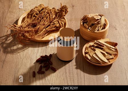 Holzschale und Teller gefüllt mit Bai Zhu und Angelica Wurzel mit mehreren roten Pillen. Arzneimittelflasche ohne Marke für Modellmarken Stockfoto