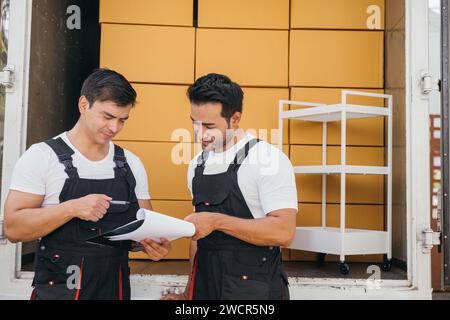 Arbeiter in einheitlichen Ausladeboxen im Freien und Checkliste für das Umzugsunternehmen. Ihre Stockfoto