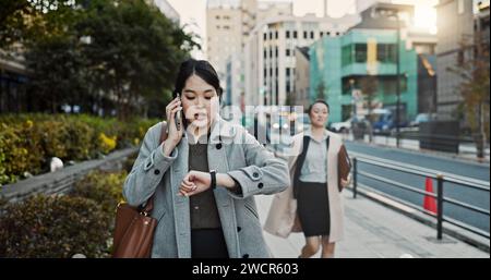 Telefonanruf, Uhr und japanische Geschäftsfrau in der Stadt, spät zur Arbeit auf der Straße oder dem Bürgersteig in Tokio. Stress, Zeit und Zeitplan mit jungen Profis Stockfoto