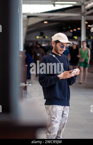 Bild eines Indianers, der ein schwarzes Kleid trägt, eine Mütze und Sonnenschirme, die auf das Telefon schauen Stockfoto