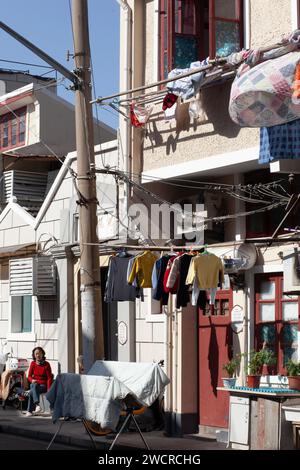 Eine Dame, die sich in ihrer Gasse entspannt, während die Wäsche in der Altstadt von Shanghai trocknet. Stockfoto