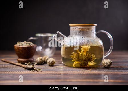 Teekanne und Glasbecher mit blühender Teeblüte auf einem Holztisch Stockfoto