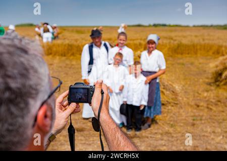 Der Fotograf hält eine Fotokamera, er macht Fotos, betrachtet die Kamera der Familie in weißen Volkstrachten, wie sie im Weizenfeld steht und posiert Stockfoto