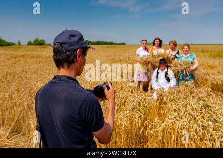 Der Fotograf hält eine Fotokamera, er macht Fotos, betrachtet die Kamera der Familie in weißen Volkstrachten, wie sie im Weizenfeld steht und posiert Stockfoto