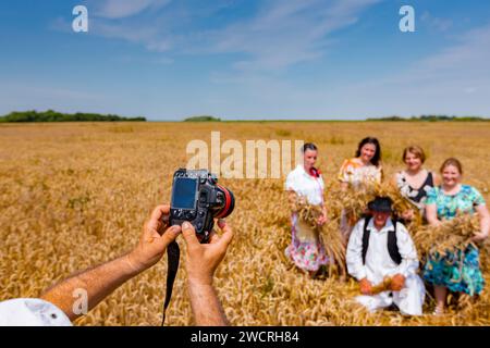 Der Fotograf hält eine Fotokamera, er macht Fotos, betrachtet die Kamera der Familie in weißen Volkstrachten, wie sie im Weizenfeld steht und posiert Stockfoto