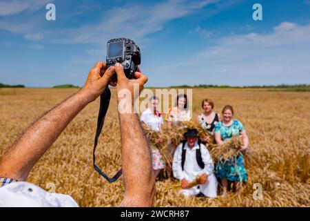 Der Fotograf hält eine Fotokamera, er macht Fotos, betrachtet die Kamera der Familie in weißen Volkstrachten, wie sie im Weizenfeld steht und posiert Stockfoto