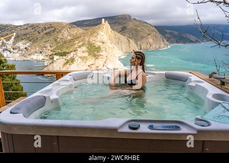 Nehmen Sie sich Zeit für sich. Badesachen im Freien mit Blick auf die Berge und das Meer. Eine Frau im schwarzen Badeanzug entspannt sich im Hotelpool und bewundert die Aussicht Stockfoto