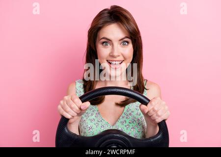 Foto von aufgeregten fröhlichen süßen Mädchen tragen stilvolle Kleidung, die ein eigenes schnelles Auto fährt isoliert auf rosa Hintergrund Stockfoto