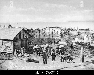 Eine Fotografie von 1901, die in Fort Resolution am Great Slave Lake in den Northwest Territories von C W Mathers auf einer Expedition in den hohen Norden Kanadas aufgenommen und in seinem Buch „The Far North“ veröffentlicht wurde. Mathers untertitelte dieses Foto: Indianer, die Waren vom Ufer des Great Slave Lake bei Resolution packen. Stockfoto