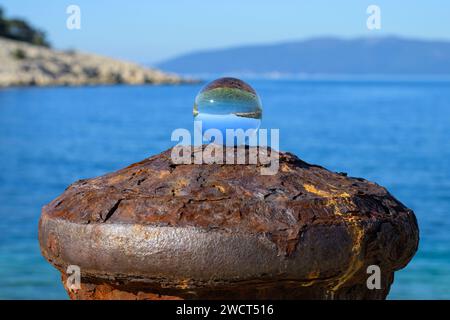 Glaskugel liegt auf einem rostigen Poller, sonniger Herbsttag in Cres (Kroatien), Meer und blauer Himmel Stockfoto