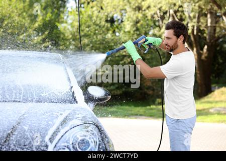 Mann, der das Auto mit Schaum in der Autowaschanlage im Freien bedeckt Stockfoto