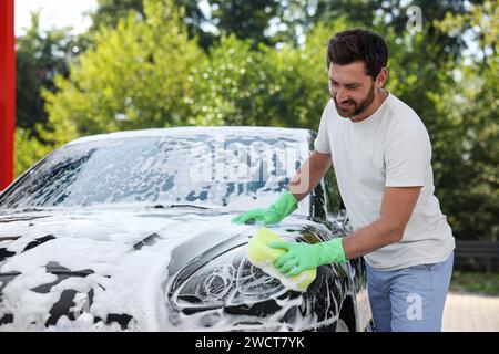 Glücklicher Mann, der draußen Auto mit Schwamm wäscht Stockfoto