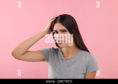 Emotionale Frau, die ihr Haar und ihre Kopfhaut auf rosa Hintergrund untersucht Stockfoto