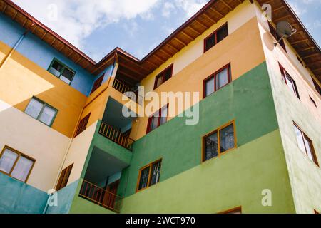 Ein flacher Blick auf ein farbenfrohes Apartmentgebäude mit gelben, grünen und blauen Wänden und Holzbalkonen unter klarem blauem Himmel Stockfoto
