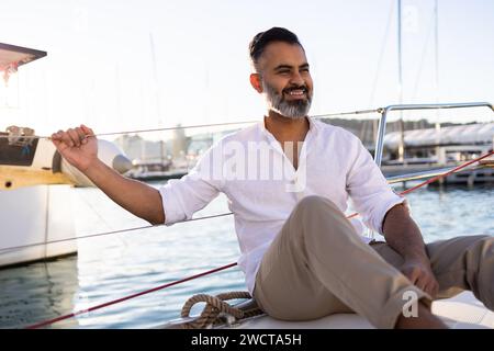 Lächelnder männlicher Reisender in legeren Kleidern, der während der Reise auf einer Yacht schwimmt, die auf plätscherndem Meerwasser schwimmt Stockfoto