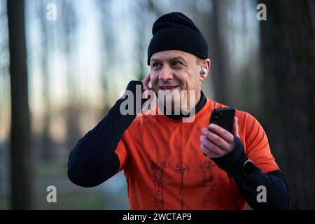 Läufer, der während des Laufens einen Anruf über Kopfhörer entgegennimmt oder Musik auflegt Stockfoto