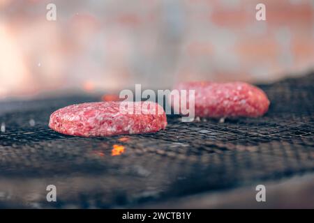 Zwei rohe Hamburger Pasteten kochen auf einem Grill über glühenden Kohlen und fangen das Wesen des Grillens ein Stockfoto