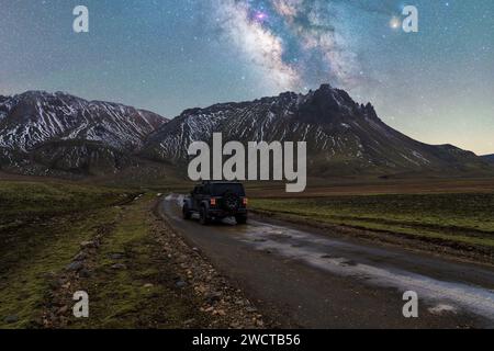 Geländewagen parkt auf einem Schotterweg mit einer Kulisse aus schneebedeckten Bergen unter der Milchstraße in Island bei Nacht Stockfoto