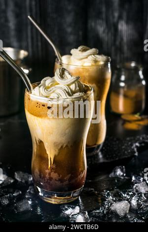 Eine verführerische griechische Frappe mit Schlagsahne auf der Oberseite, serviert in einem hohen Glas, umgeben von Eiswürfeln, die eine perfekte Mischung für einen heißen S Stockfoto