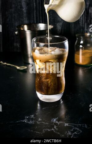 Ein verführerisches Glas griechischer Frappe in der Mitte der Zubereitung, mit einem Milchstrahl, der in der Kombination aus Instantkaffee einen wunderschönen Strudel erzeugt Stockfoto