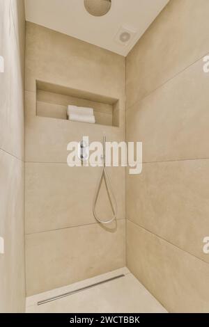 Innenblick auf eine moderne Dusche in schlichtem beigefarbenem Farbschema, mit eleganten Armaturen und einer Nische für Annehmlichkeiten. Stockfoto