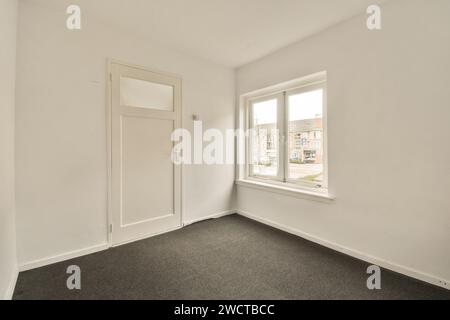 Ein leerer Raum mit einem großen Fenster, frisch bemalten Wänden und einer geschlossenen weißen Tür, die ein Gefühl des Potenzials für neue Gäste vermittelt. Stockfoto
