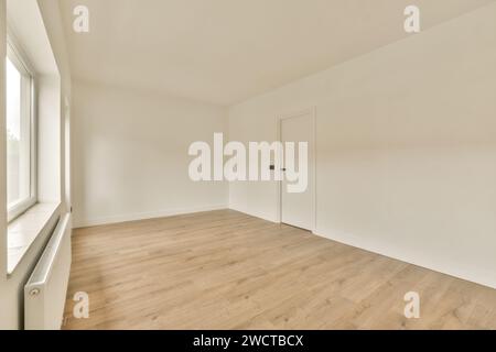 Ein geräumiger, leerer Raum mit großem Fenster, cremefarbenen Wänden und Laminatfußboden, beleuchtet durch Tageslicht. Stockfoto