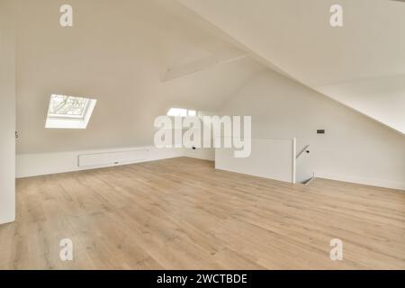 Ein leerer Dachraum mit großen Oberlichtern, modernem Holzfußboden und weißen Wänden, der einen hellen und luftigen Raum bietet. Stockfoto