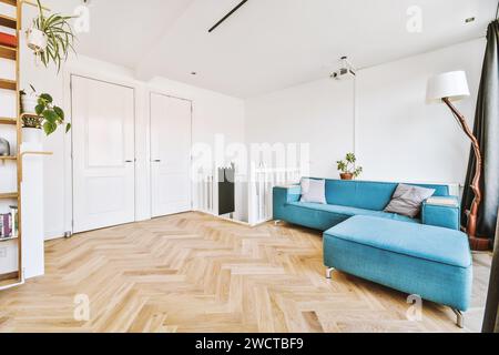 Ein helles, luftiges Wohnzimmer mit einem weichen blauen Sofa, Holzboden mit Fischgrätmuster und modernen Möbeln. Stockfoto