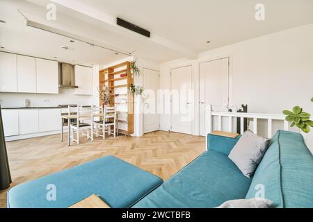Geräumiges, hell beleuchtetes Wohnzimmer, das nahtlos mit einer modernen weißen Küche verbunden ist, mit stilvollen Möbeln und Hartholzböden. Stockfoto