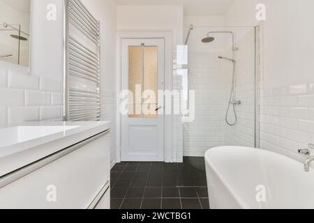 Das elegante und moderne weiße Badezimmer verfügt über eine freistehende Badewanne, eine begehbare Dusche und einen minimalistischen Kosmetikbereich mit schwarzen Bodenfliesen. Stockfoto