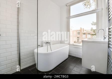 Ein sauberes, modernes Badezimmer mit weißen U-Bahn-Fliesen, einer eigenständigen Badewanne und einem großen Fenster, das viel Tageslicht ermöglicht. Stockfoto
