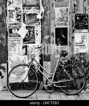 Ein Vintage-Retro-Fahrrad lehnt sich an ein Poster und eine mit Graffiti bedeckte Wand Stockfoto