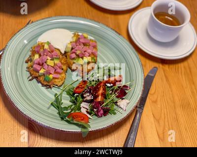 Gourmet-Kartoffelpfannkuchen mit Schinken und Avocado, serviert mit Salat und Espresso. Stockfoto