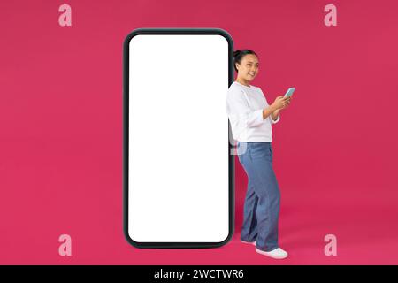 Tolle App. Asiatische Frau, Die Smartphone Benutzt Und Sich An Das Große Leere Handy Lehnt Stockfoto