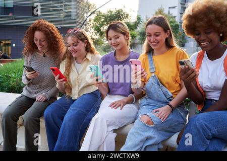Multirassische Gruppe junger Freundinnen, die ihre Handys im Freien benutzen und lächeln. Stockfoto