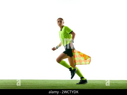 Schiedsrichterassistent, junge Frau in Uniform in Bewegung auf dem Feld, läuft mit Flagge, führt die Kontrolle über das Spiel vor weißem Studiohintergrund Stockfoto