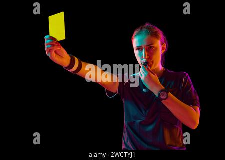 Disziplinarmaßnahmen. Weibliche Schiedsrichterin zeigt gelbe Karte vor schwarzem Studiohintergrund im Neonlicht. Spielregeln befolgen Stockfoto