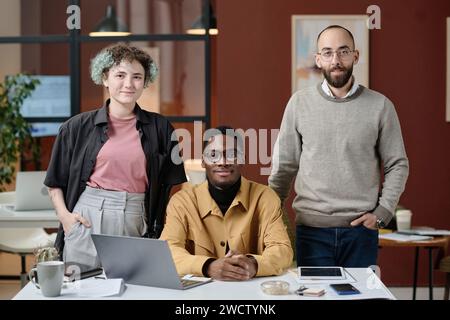 Zwei männliche Kollegen und ihre weibliche Kollegin posieren am Schreibtisch und lächeln in die Kamera Stockfoto